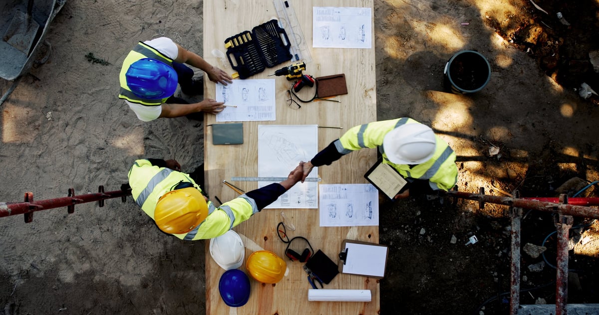 Construction team reviewing blueprints and shaking hands on a project agreement